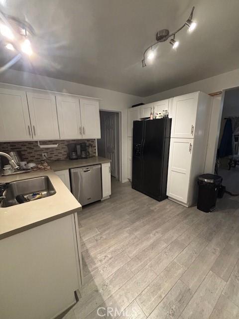 kitchen featuring black fridge, dishwasher, white cabinets, light hardwood / wood-style flooring, and sink