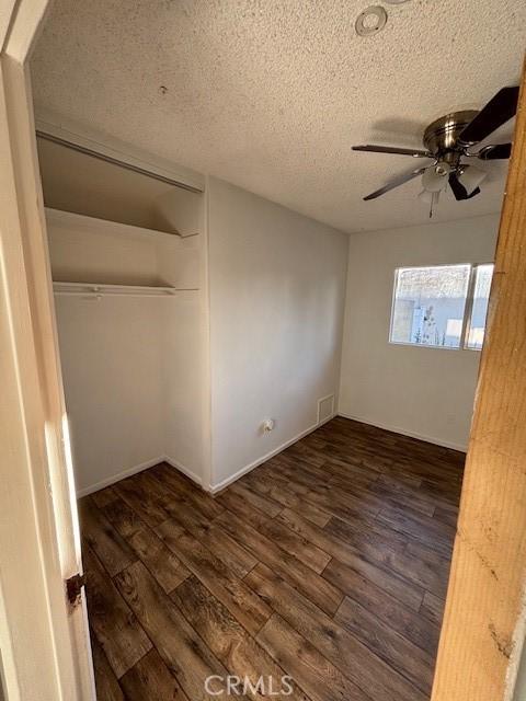 unfurnished bedroom with dark wood-type flooring, ceiling fan, a closet, and a textured ceiling