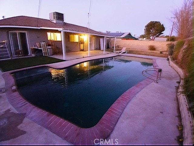 pool at dusk with a patio area and cooling unit