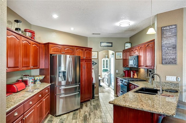 kitchen featuring light hardwood / wood-style floors, kitchen peninsula, sink, hanging light fixtures, and appliances with stainless steel finishes