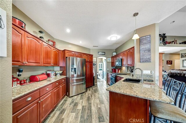 kitchen featuring pendant lighting, appliances with stainless steel finishes, light hardwood / wood-style floors, sink, and kitchen peninsula