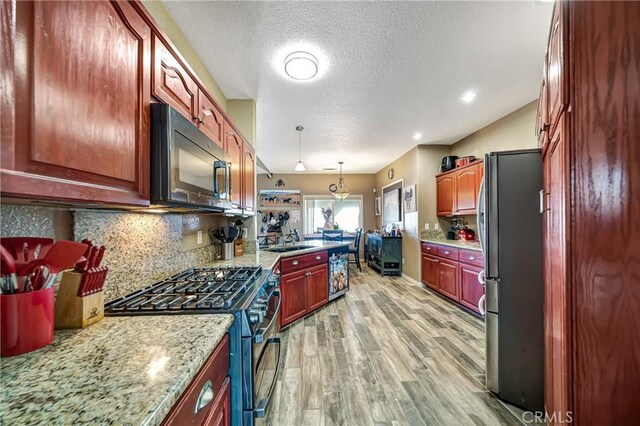 kitchen with stainless steel appliances, hanging light fixtures, light hardwood / wood-style flooring, light stone counters, and sink