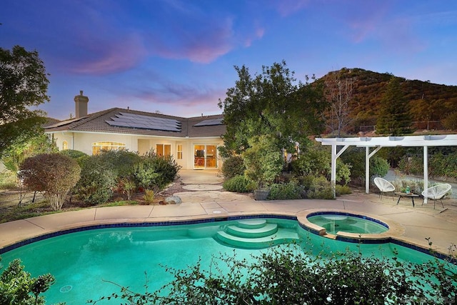 pool at dusk featuring a mountain view, a patio area, and an in ground hot tub