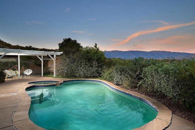 pool at dusk featuring an in ground hot tub, a mountain view, and a patio