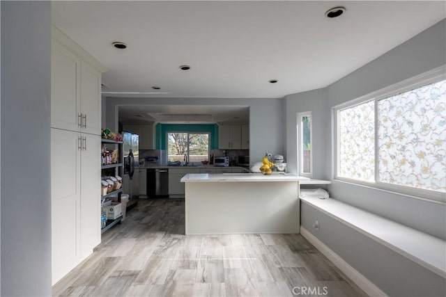 kitchen with dishwasher, kitchen peninsula, stainless steel refrigerator with ice dispenser, sink, and white cabinetry