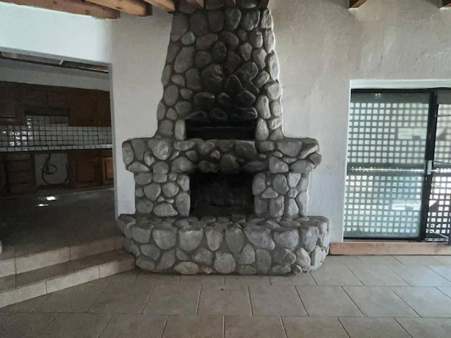 unfurnished living room featuring beam ceiling, light tile patterned floors, and a stone fireplace