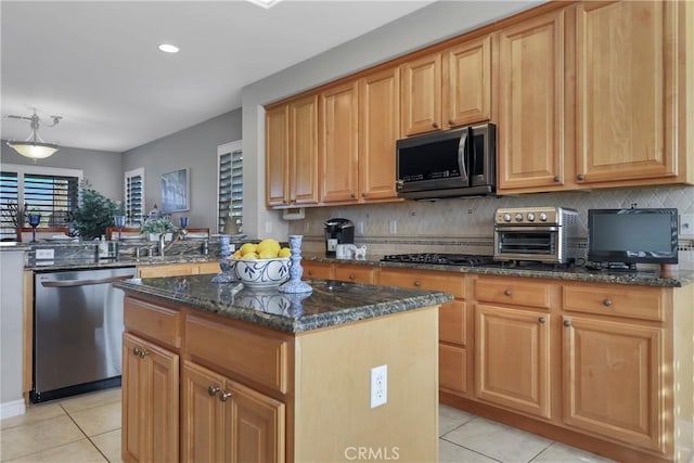 kitchen with light tile patterned floors, dishwasher, dark stone countertops, and a kitchen island