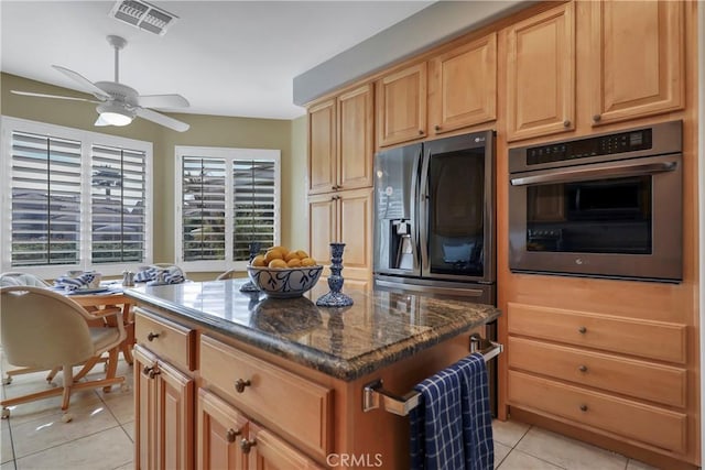 kitchen with ceiling fan, a kitchen island, light tile patterned flooring, stainless steel appliances, and dark stone counters