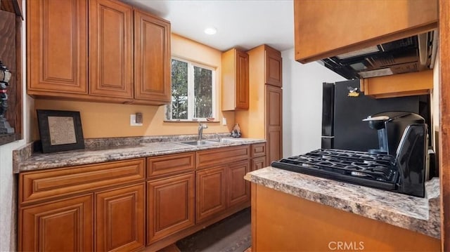 kitchen with light stone countertops, sink, black fridge, ventilation hood, and stove