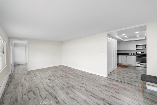 unfurnished living room with light hardwood / wood-style floors and a raised ceiling