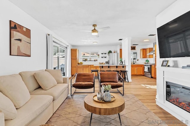 living room with ceiling fan, sink, and light hardwood / wood-style floors