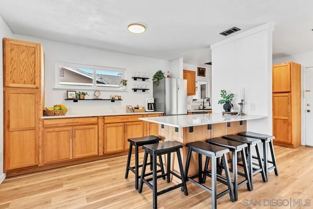 kitchen with a breakfast bar, sink, light hardwood / wood-style flooring, stainless steel fridge, and kitchen peninsula