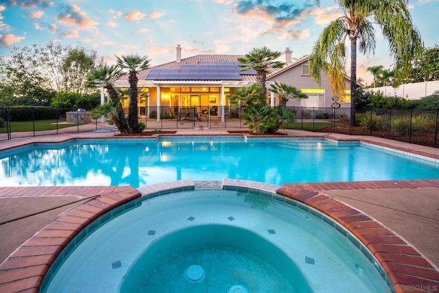 pool at dusk with an in ground hot tub and a patio area