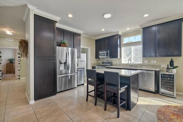 kitchen featuring a kitchen island, appliances with stainless steel finishes, wine cooler, light tile patterned floors, and crown molding