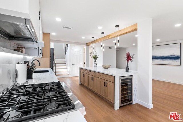 kitchen featuring light stone countertops, beverage cooler, decorative light fixtures, sink, and light wood-type flooring