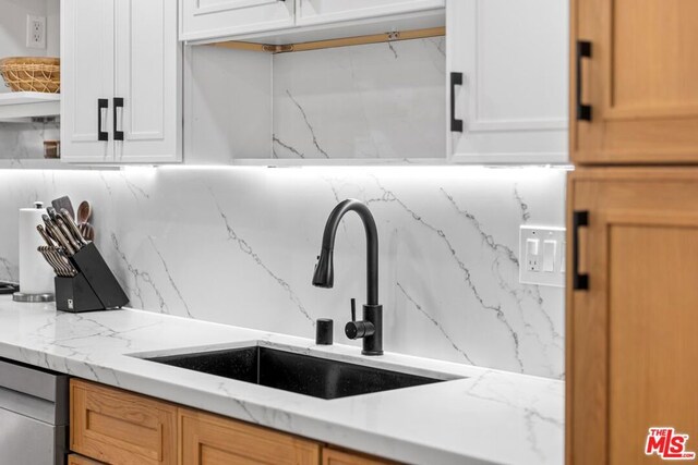 interior details featuring light stone countertops, sink, white cabinetry, and tasteful backsplash