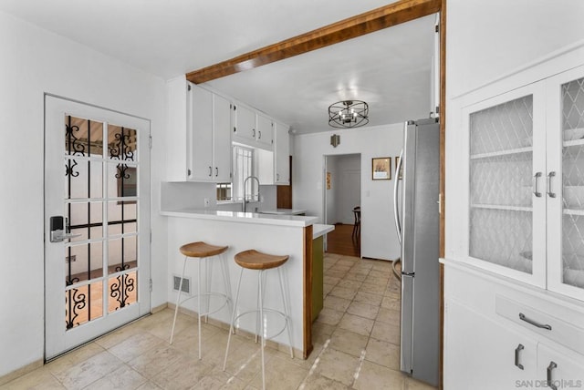 kitchen with white cabinetry, a kitchen breakfast bar, sink, kitchen peninsula, and stainless steel refrigerator