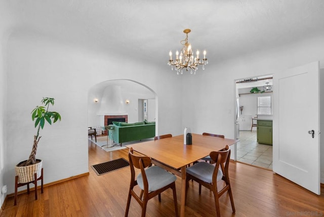 dining room with light wood-type flooring, a brick fireplace, and a notable chandelier