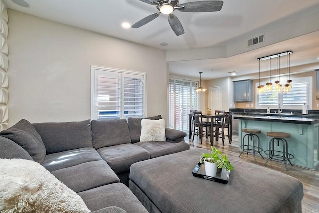 living room with ceiling fan with notable chandelier, plenty of natural light, and light hardwood / wood-style floors