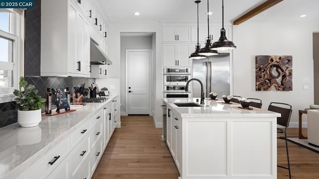 kitchen featuring a breakfast bar area, stainless steel appliances, decorative light fixtures, a kitchen island with sink, and white cabinets