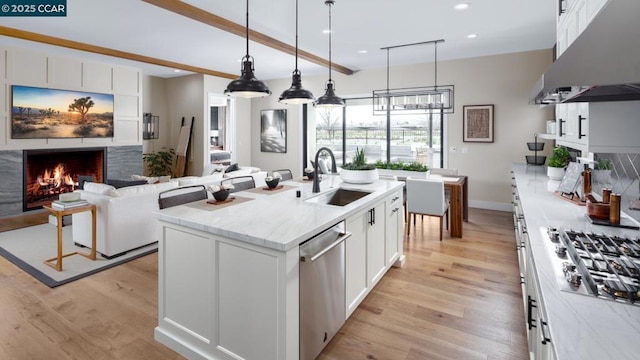 kitchen featuring light stone countertops, appliances with stainless steel finishes, white cabinetry, sink, and a center island with sink