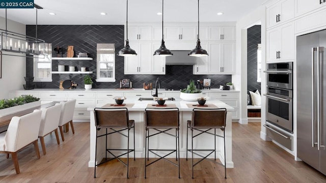 kitchen featuring tasteful backsplash, white cabinets, a kitchen island with sink, and pendant lighting