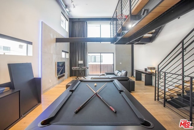 recreation room featuring light wood-type flooring, a tiled fireplace, pool table, and a towering ceiling