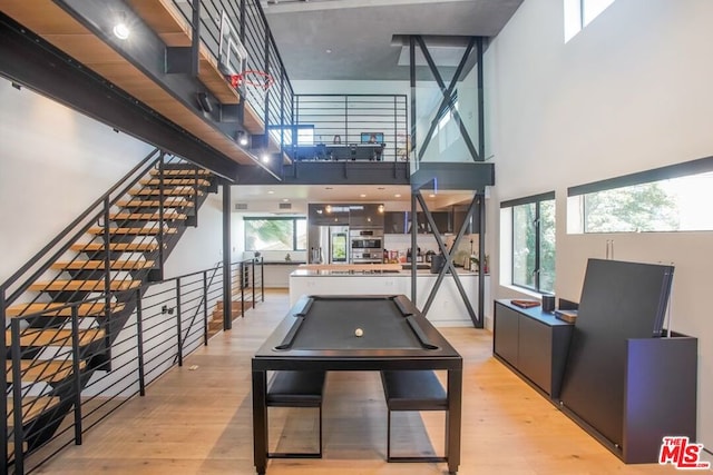 playroom with a towering ceiling, pool table, and light hardwood / wood-style flooring