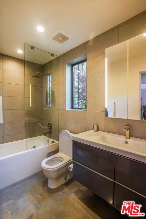 full bathroom featuring toilet, vanity, tile walls, shower / washtub combination, and concrete floors