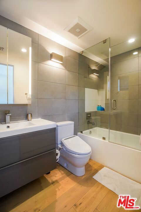 full bathroom featuring wood-type flooring, vanity, tile walls, toilet, and combined bath / shower with glass door