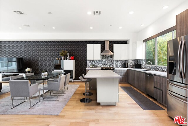 kitchen featuring appliances with stainless steel finishes, dark brown cabinets, a kitchen island, wall chimney exhaust hood, and white cabinets