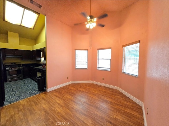 kitchen featuring ceiling fan, sink, hardwood / wood-style flooring, stainless steel gas range, and high vaulted ceiling