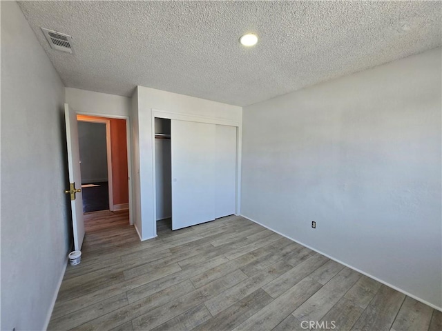 unfurnished bedroom with a textured ceiling, a closet, and light hardwood / wood-style flooring