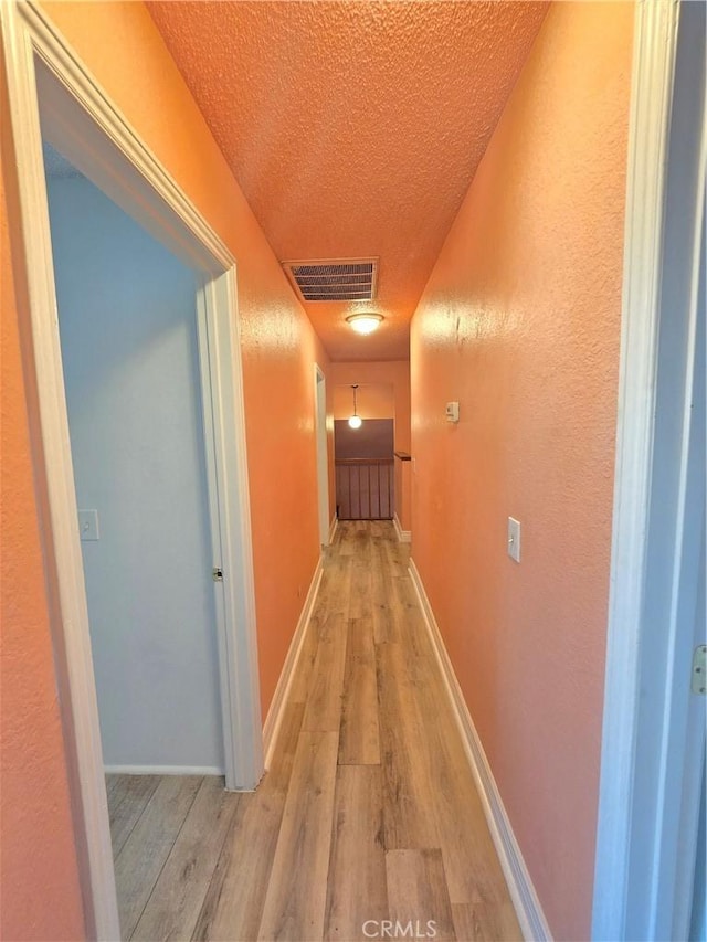 hallway with a textured ceiling and light wood-type flooring