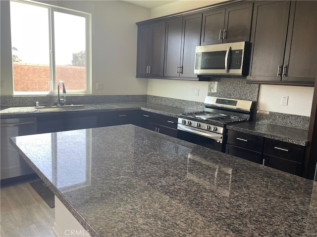 kitchen featuring dark stone counters, sink, stainless steel appliances, and dark brown cabinetry