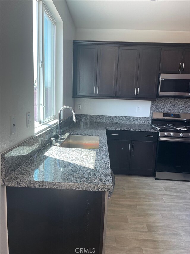 kitchen featuring light hardwood / wood-style floors, sink, stainless steel appliances, and dark stone countertops