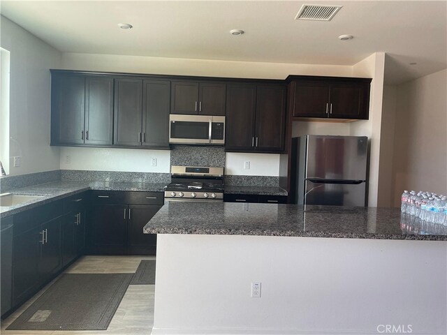 kitchen with stainless steel appliances, dark stone counters, and sink