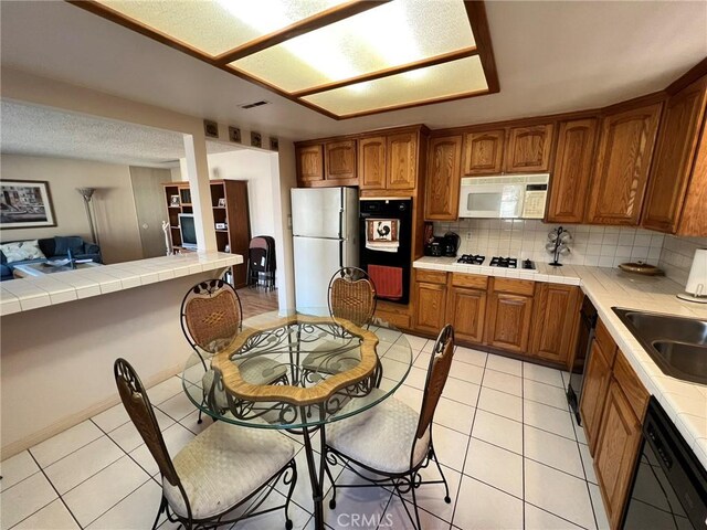 kitchen featuring tile counters, light tile patterned floors, decorative backsplash, and white appliances