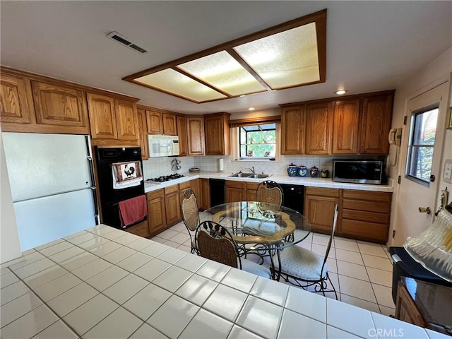 kitchen with light tile patterned floors, tile countertops, backsplash, black appliances, and sink