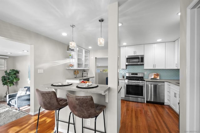 kitchen with white cabinetry, stainless steel appliances, dark hardwood / wood-style floors, and a kitchen bar