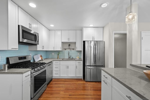 kitchen featuring white cabinetry, sink, hanging light fixtures, stainless steel appliances, and light hardwood / wood-style flooring