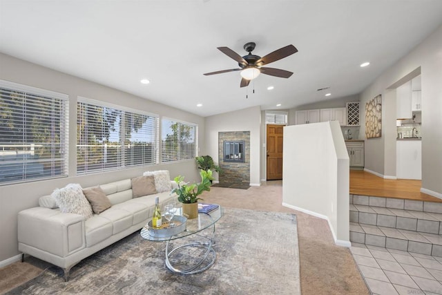 living room with ceiling fan, light colored carpet, a stone fireplace, and vaulted ceiling