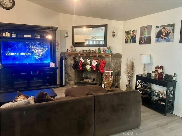 living room with lofted ceiling, hardwood / wood-style flooring, and a stone fireplace