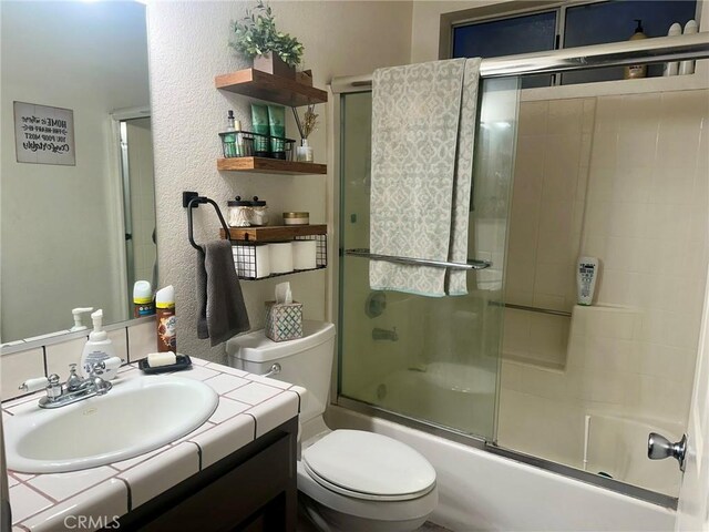 full bathroom with toilet, bath / shower combo with glass door, and vanity