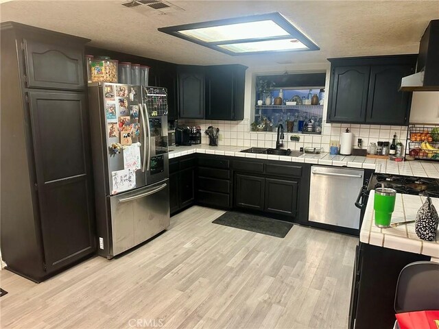 kitchen with appliances with stainless steel finishes, tile countertops, decorative backsplash, and light hardwood / wood-style flooring