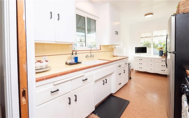 kitchen with white cabinets, tile counters, decorative backsplash, sink, and stainless steel fridge