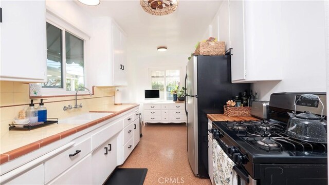 kitchen featuring tile counters, backsplash, stainless steel gas stove, white cabinets, and sink