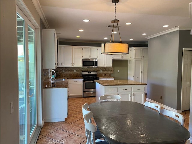 kitchen with white cabinets, appliances with stainless steel finishes, a kitchen island, sink, and hanging light fixtures