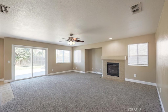 unfurnished living room featuring a textured ceiling, ceiling fan, light colored carpet, and a tiled fireplace