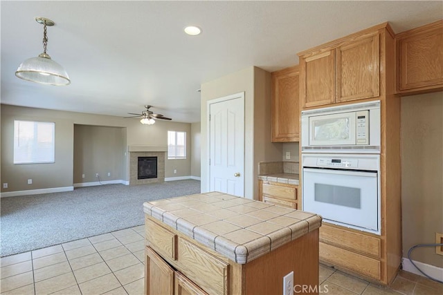 kitchen with pendant lighting, white appliances, a center island, tile countertops, and light colored carpet